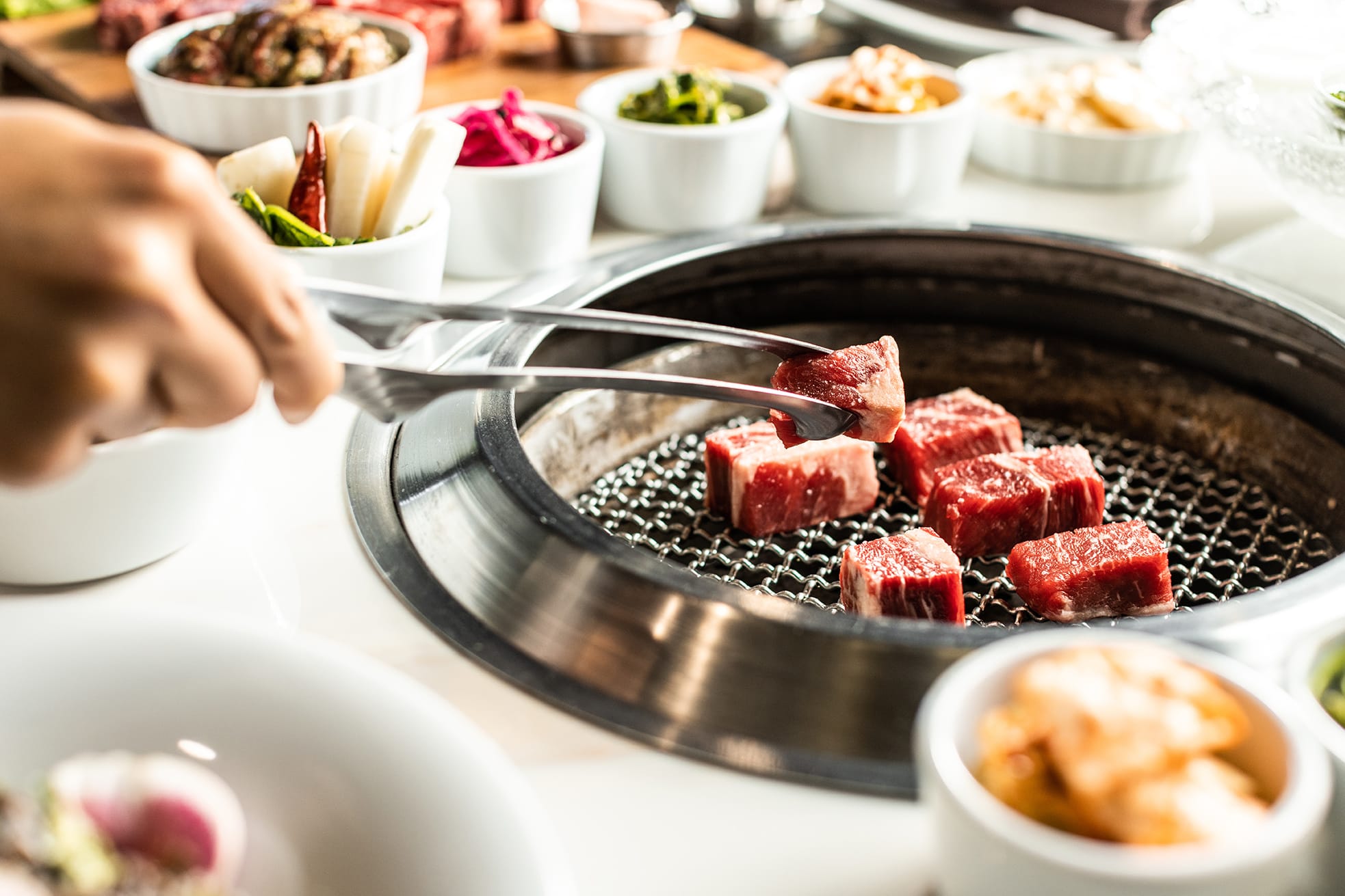 fresh steak being grilled with korean side dishes