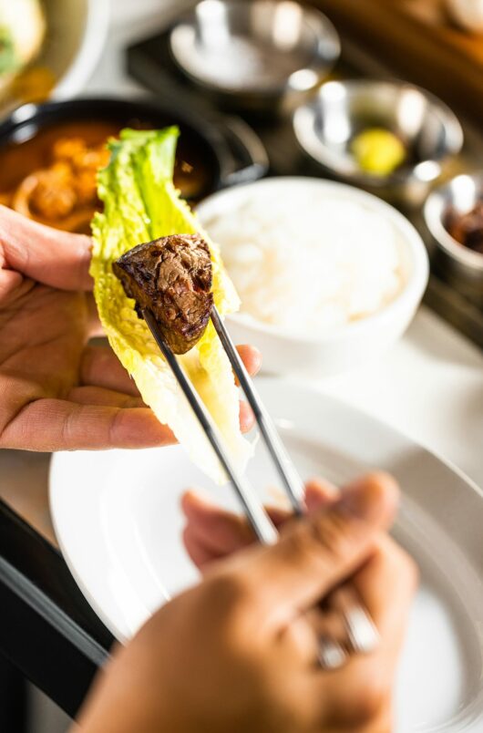 customer using chopsticks to combine korean barbecue sides with steak